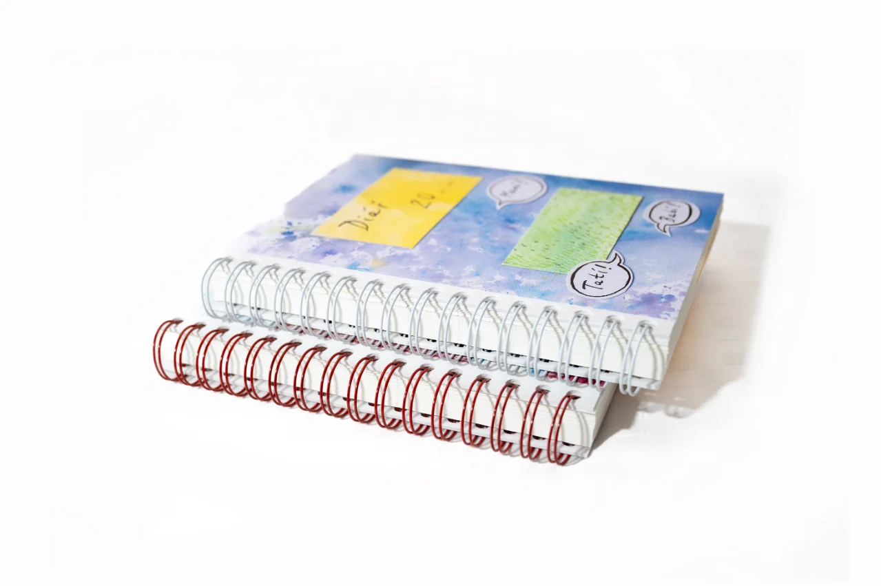 Dva nedatované diáře Čáromat v modré a červené barvě, pohled z boku na kroužkovou vazbu.